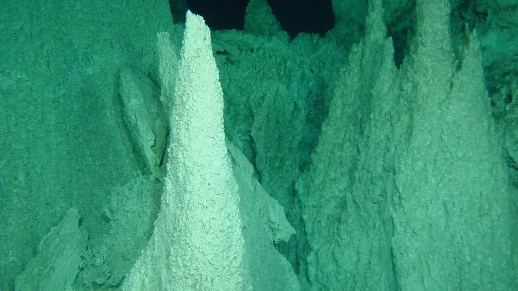 Maciço de chaminés de carbonato fotografado a 750-900 metros de profundidade no Lost City Hydrothermal Field, no Atlântico Norte. Estruturas tubulares brancas erguem-se do fundo oceânico, captadas por veículo submarino.