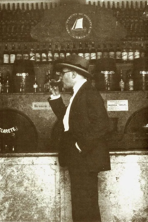 Fernando Pessoa sentado a levantar um copo de vinho no armazém Abel Pereira da Fonseca, em Lisboa, em 1928