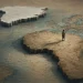 África e Gronelândia representadas em relevo sobre um mapa antigo cor-de-areia, com uma figura humana minúscula a caminhar pelo continente africano