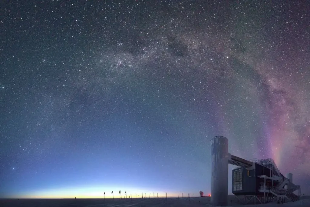Laboratório do observatório de neutrinos IceCube na escuridão do polo sul, com a faixa da Via Láctea e auroras no céu